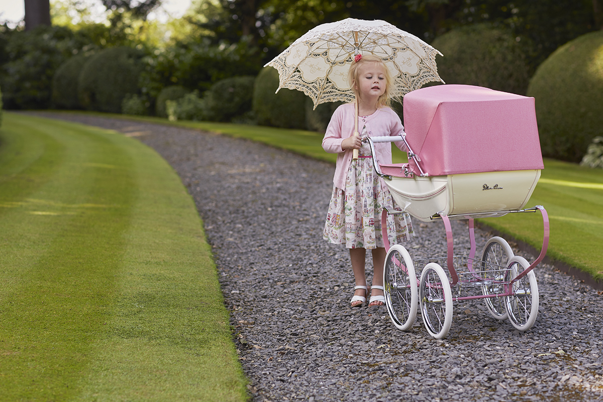 young girl playing with silver cross dolls' pram