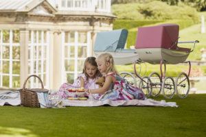 two girls having a picnic next to silver cross dolls' prams