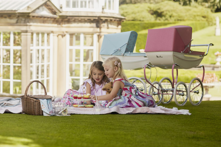 two girls having a picnic next to silver cross dolls' prams