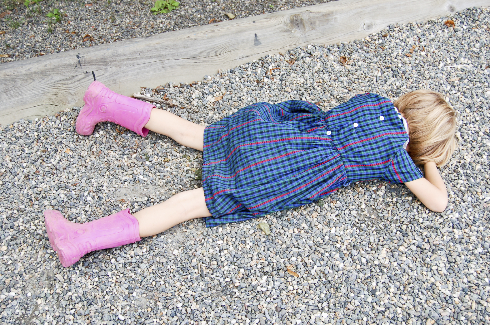 A sad child lies on the gravel of a school playground.