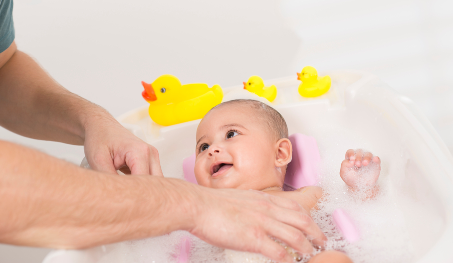 Father bathing his adorable baby girl. 3 toy duck on background.