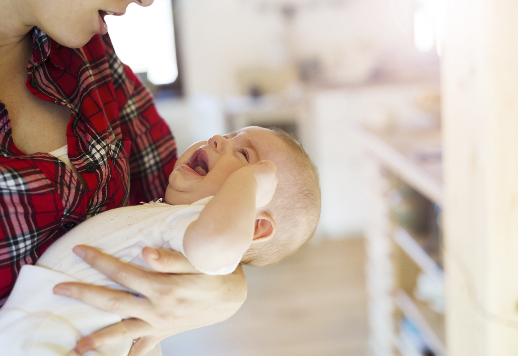 Crying little baby in the arms of her mother in a living room.