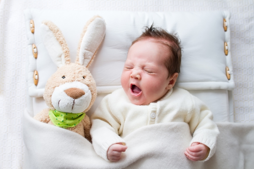 Adorable sleepy newborn baby with a toy bunny yawning in bed
